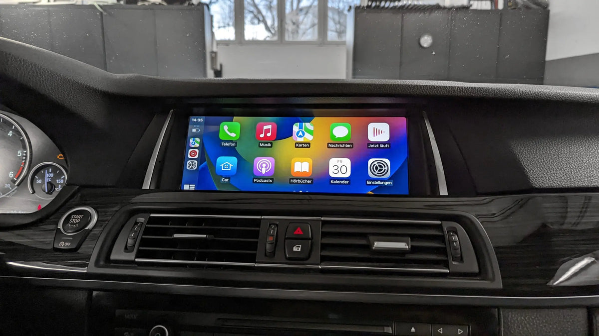 A close-up of a bmw f10 dashboard with a touchscreen display showing Apple CarPlay interface, mounted above the air vents.