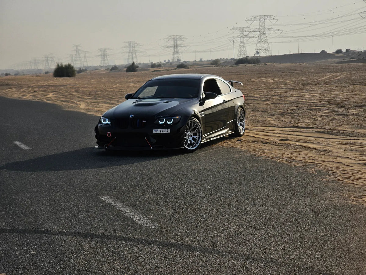 Black BMW E92 with black housing LED headlights installed, shown from a front three-quarter angle in daylight.