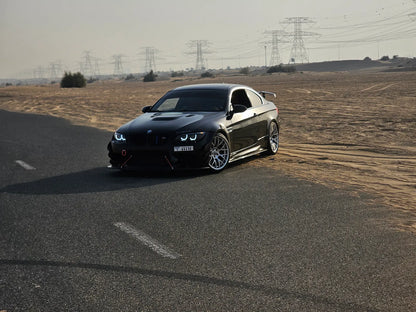 Black BMW E92 with black housing LED headlights installed, shown from a front three-quarter angle in daylight.