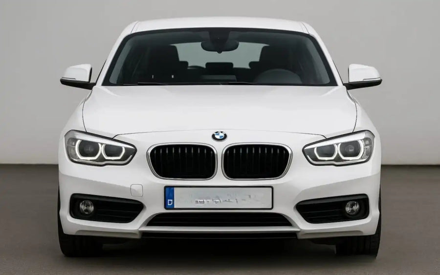 A white BMW 1 Series sedan shown from the front in a studio setting with a neutral gray background.