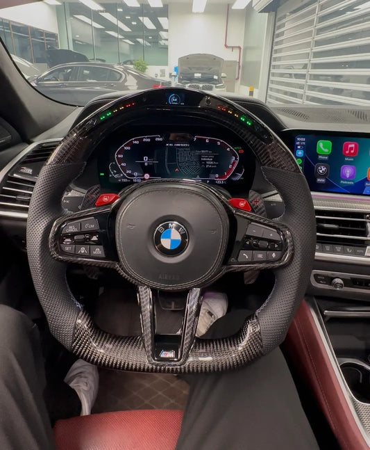 Custom carbon fiber steering wheel with LED rev limiter display and custom color lighting installed in a BMW G Series interior