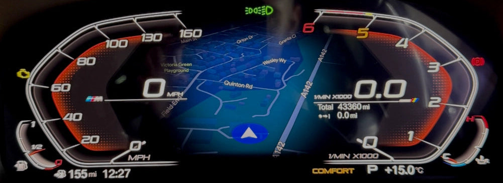 A close-up of a BMW's illuminated digital instrument cluster display, showing a blue navigation map, speedometer, tachometer, and vehicle status indicators on a dark dashboard.