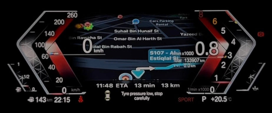 A close-up of a BMW digital instrument cluster display on a motorcycle, showing navigation details, speed, fuel level, and vehicle status on a black background.