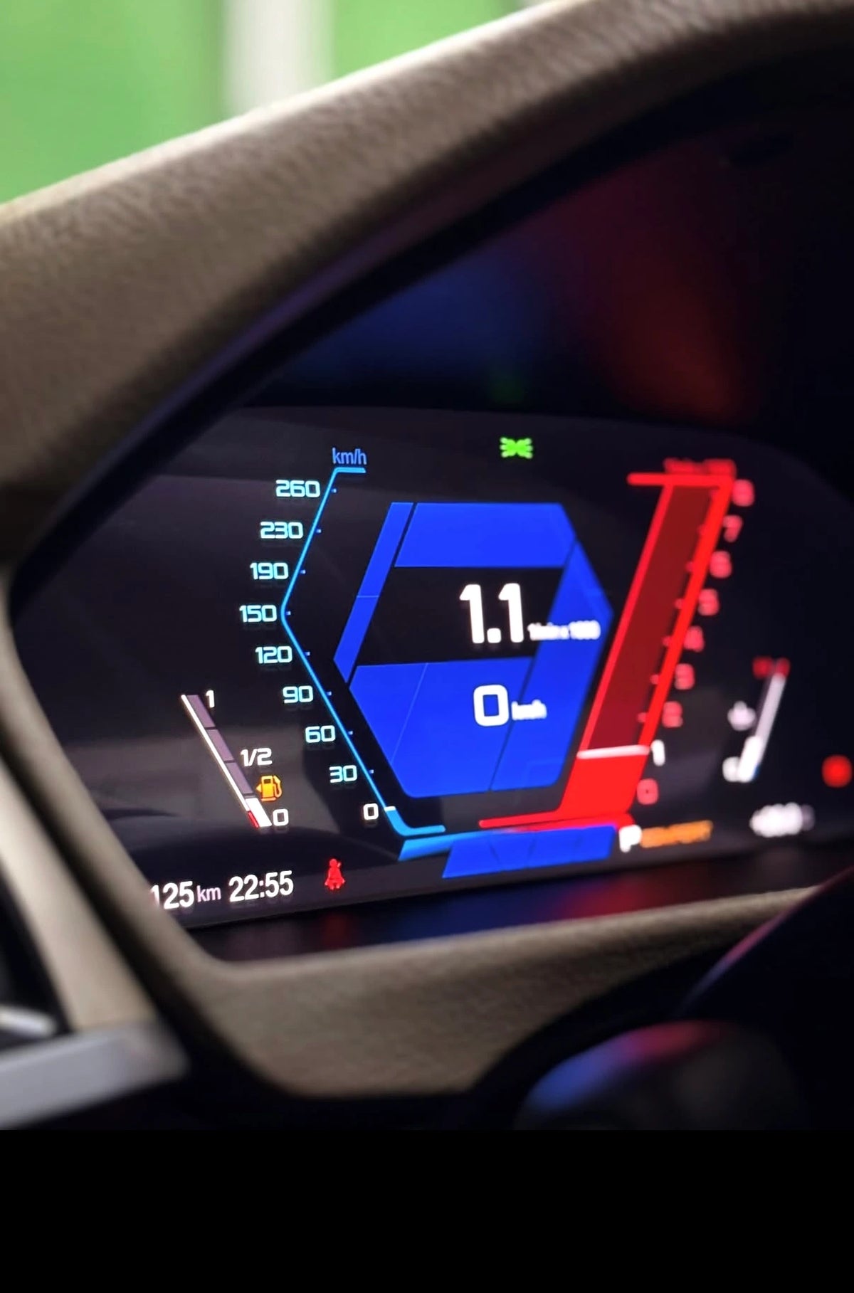 Close-up of a BMW's digital instrument cluster display showing a blue and red dashboard interface, framed by the beige leather steering wheel.