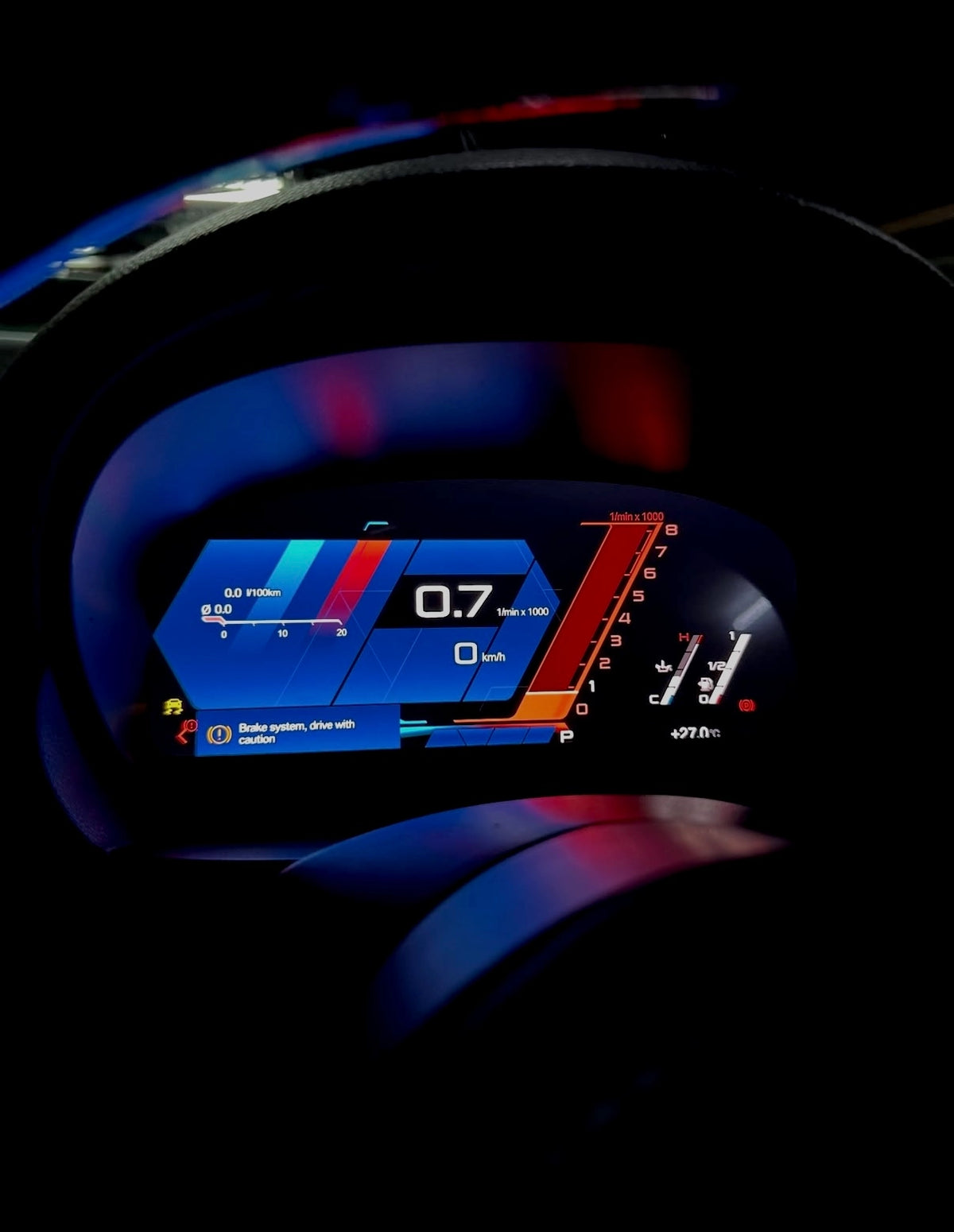 A close-up of a BMW's digital instrument cluster display upgrade illuminated in dark tones, showing blue, red, and orange dashboard graphics and vehicle metrics.