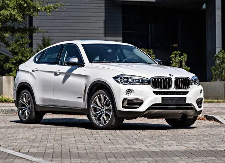 A white BMW X6 F16 SUV parked on a paved street in front of a modern gray building.