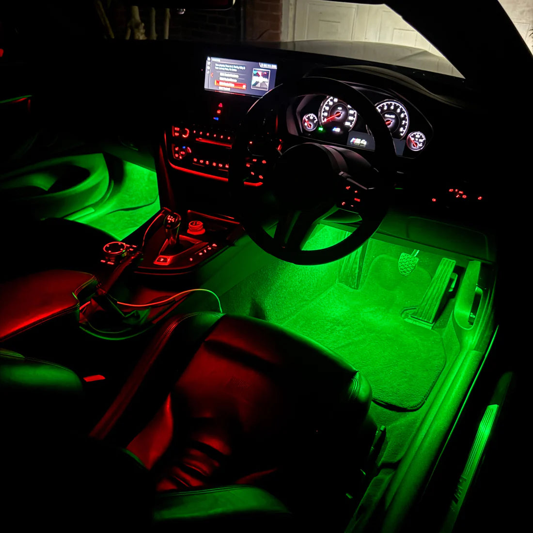 Green LED under-seat car floor lights illuminating the driver's footwell and center console in a black car interior.
