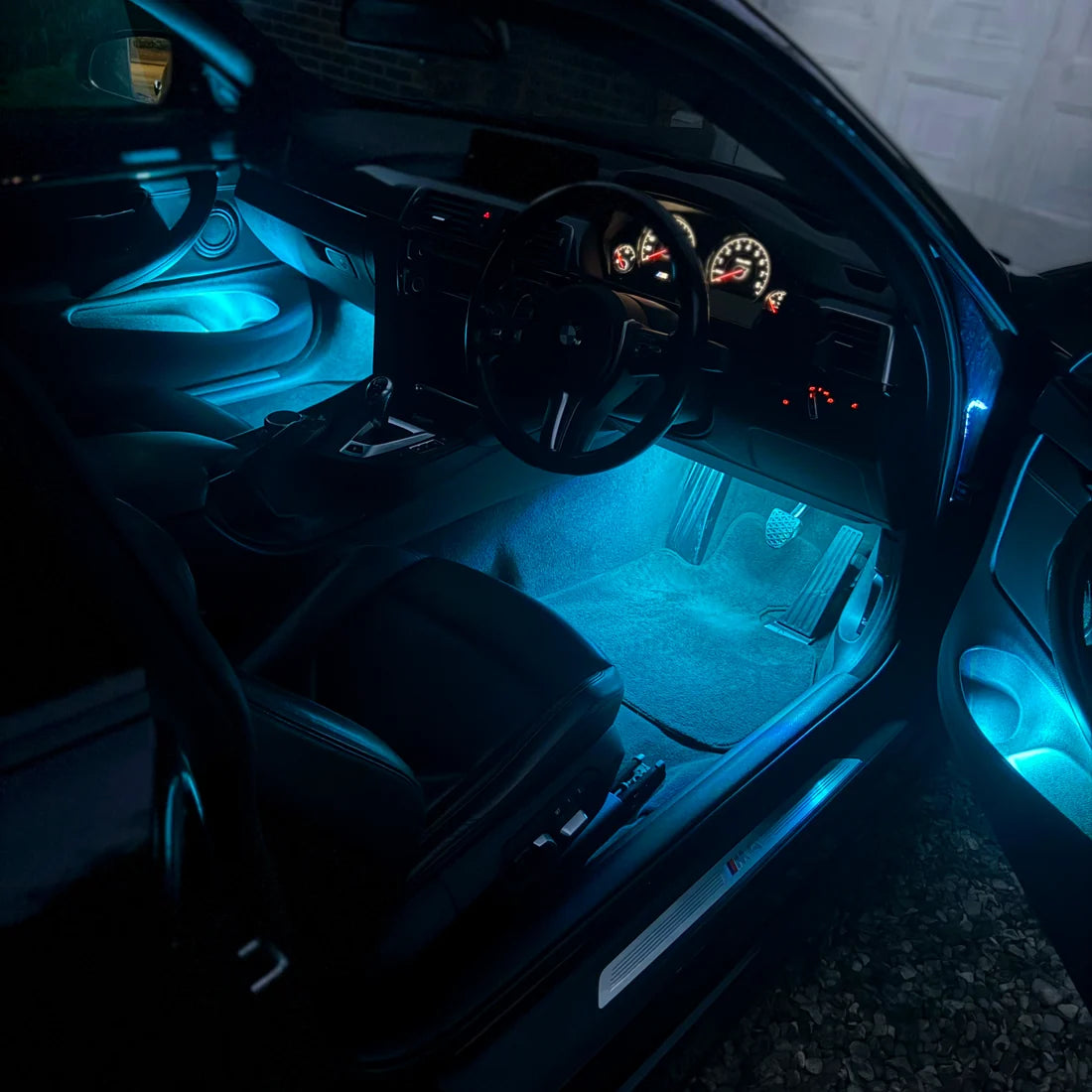 Blue LED underdoor car light illuminated inside a black car, casting a bright cyan glow onto the footwell and interior floor mat.